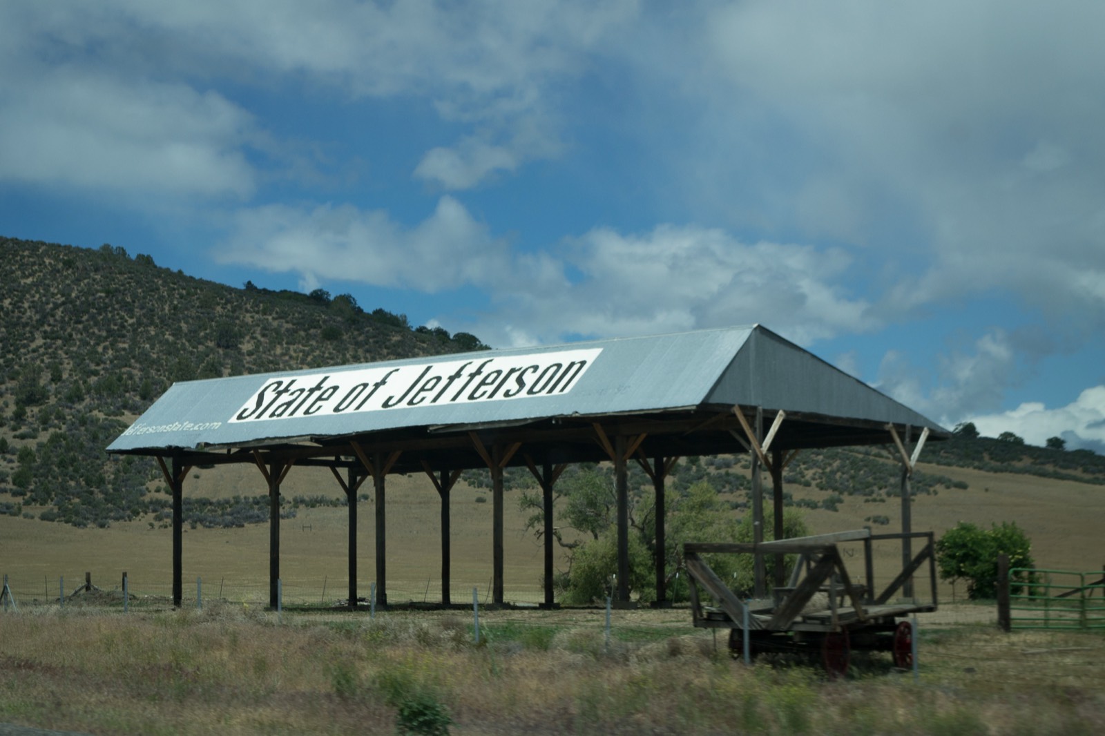 Metal-roofed hay barn in a dry valley near Yreka with 'State of Jefferson' painted in large letters on the roof, brushy hillside behind